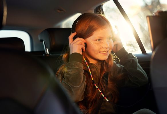 Ung jente ser på skjerm med hodetelefoner bak i en bil