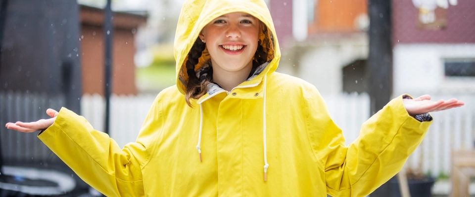 Smilende jente i gul regnjakke ute i regnvær