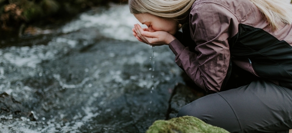 Ung kvinne i turklær drikker vann fra bekk