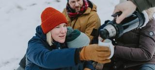 Kvinne med rød topplue får servert kaffe ute i snøen